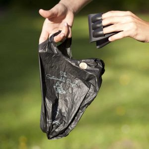 Frau benutzt einen Pooper Scooper zusammen mit einem biologisch abbaubaren Hundekotbeutel aus einem Biokunststoff mit Maisstärke